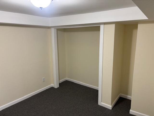 basement with baseboards and dark colored carpet