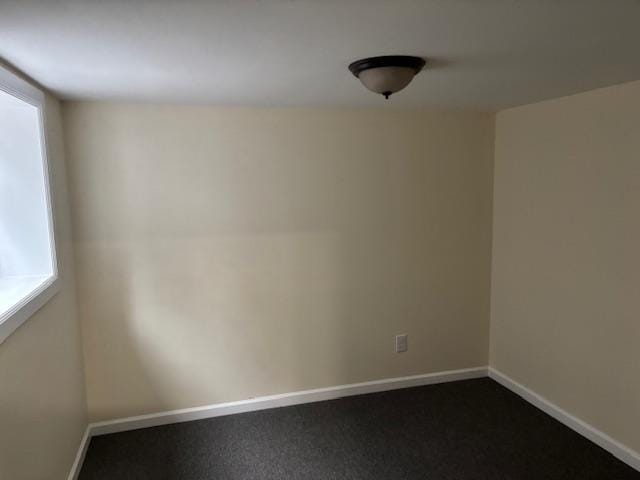 unfurnished room featuring baseboards and dark colored carpet