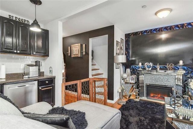 kitchen featuring tasteful backsplash, dishwasher, a glass covered fireplace, wood finished floors, and decorative light fixtures