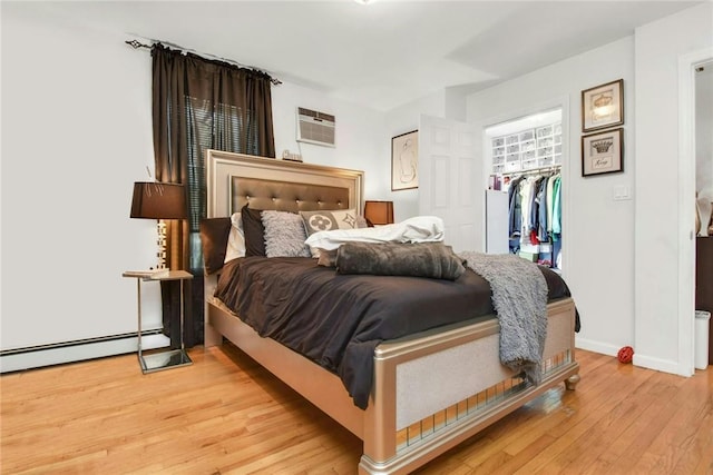 bedroom with a walk in closet, a baseboard radiator, a closet, light wood-style floors, and baseboards