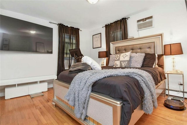 bedroom featuring an AC wall unit, baseboard heating, and wood finished floors