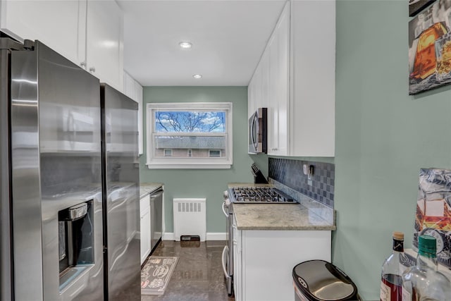 kitchen with stainless steel appliances, backsplash, radiator heating unit, white cabinetry, and light stone countertops