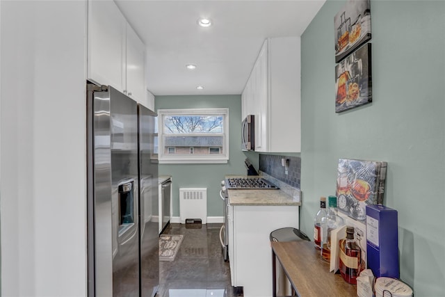 kitchen with tasteful backsplash, baseboards, white cabinets, radiator, and appliances with stainless steel finishes