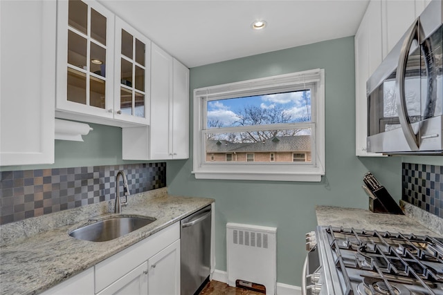 kitchen featuring stainless steel appliances, a sink, white cabinetry, radiator, and glass insert cabinets