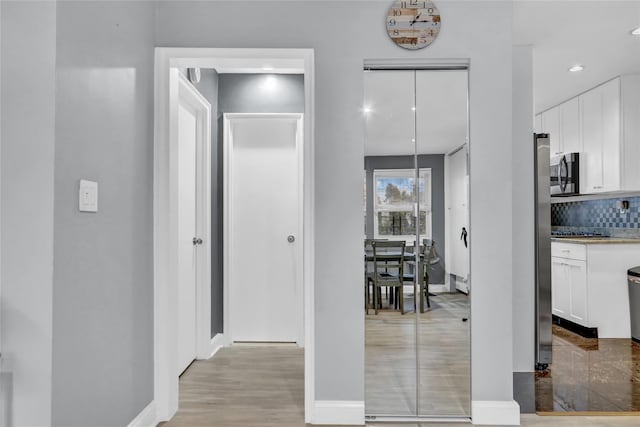 hallway featuring light wood-style flooring, baseboards, and recessed lighting