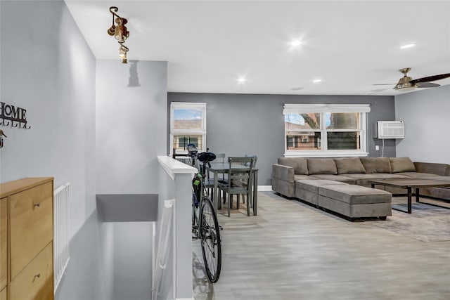 living area featuring a wall unit AC, recessed lighting, a ceiling fan, baseboards, and light wood-style floors