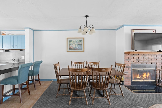 tiled dining space with crown molding, a fireplace, a notable chandelier, a sink, and baseboards