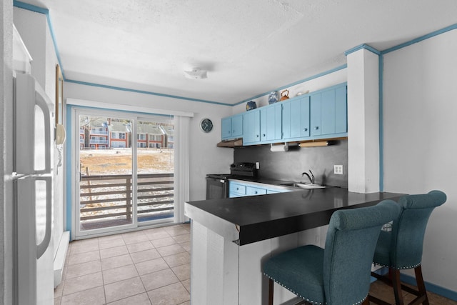 kitchen with a sink, blue cabinetry, freestanding refrigerator, stainless steel electric stove, and dark countertops