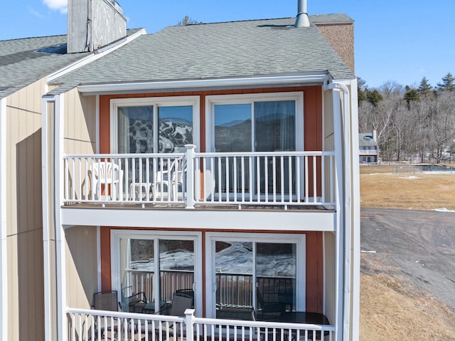 back of house with a shingled roof, a chimney, and a balcony