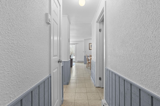 hallway with a textured wall, wainscoting, and light tile patterned flooring