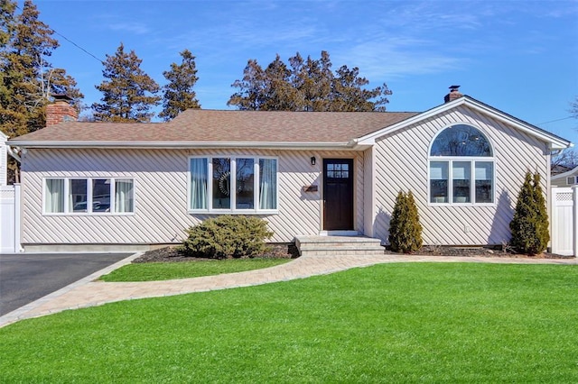 single story home featuring aphalt driveway, roof with shingles, a chimney, fence, and a front lawn