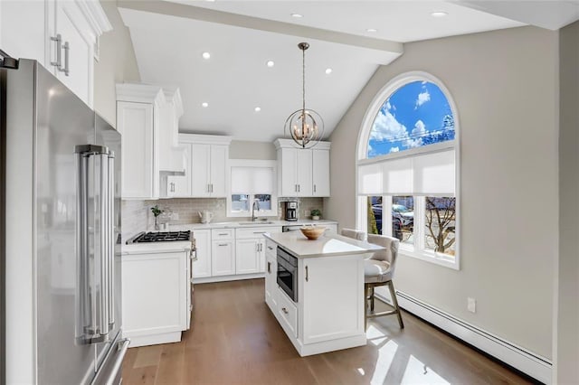 kitchen with a sink, light countertops, appliances with stainless steel finishes, baseboard heating, and decorative backsplash