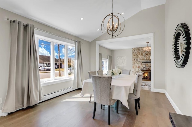 dining space with light wood finished floors, a fireplace, vaulted ceiling, and a notable chandelier