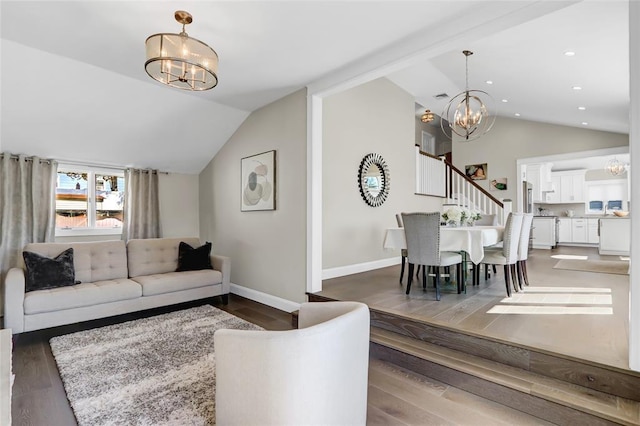 living area featuring lofted ceiling, stairway, a notable chandelier, and wood finished floors