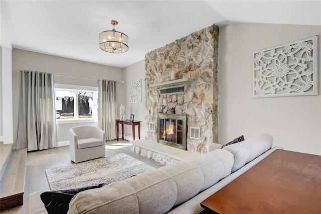 living area featuring lofted ceiling, a stone fireplace, a notable chandelier, wood finished floors, and visible vents