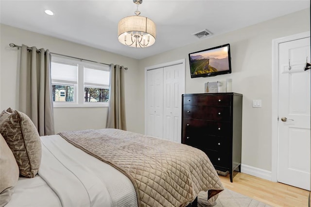 bedroom with light wood finished floors, a closet, visible vents, a chandelier, and baseboards