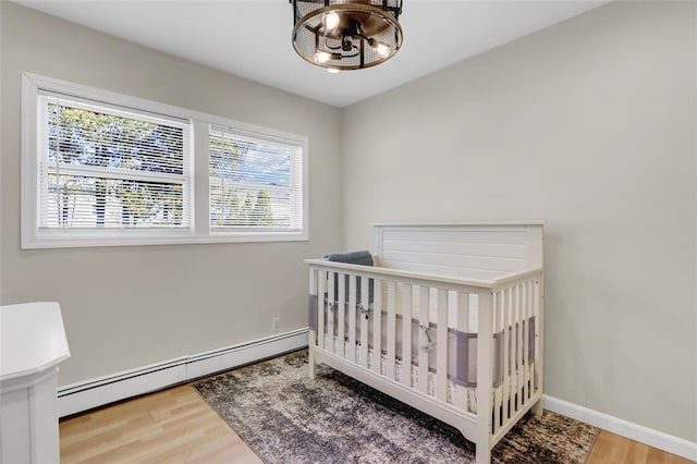 bedroom with a crib, a baseboard radiator, wood finished floors, and baseboards