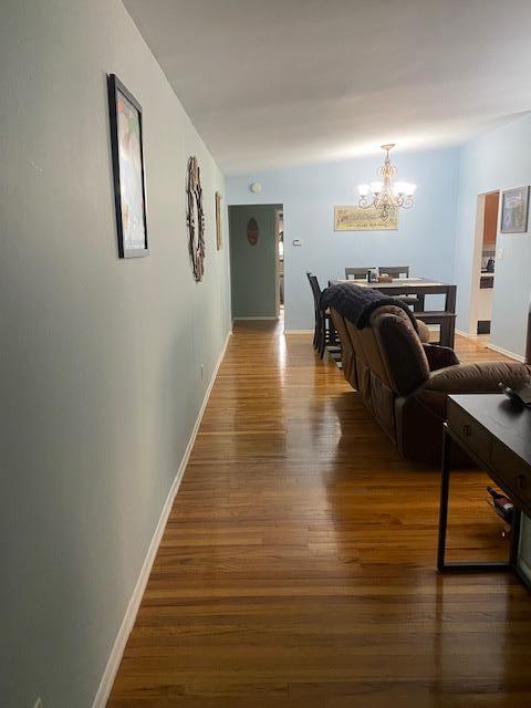 corridor featuring baseboards, wood finished floors, and an inviting chandelier