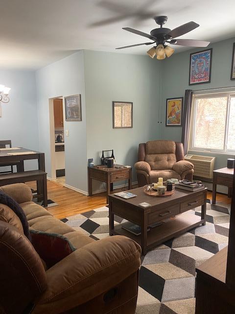 living room featuring light wood-style floors, baseboards, and ceiling fan with notable chandelier