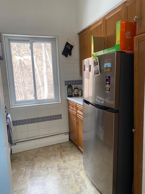 kitchen with brown cabinetry, freestanding refrigerator, light countertops, and tile walls