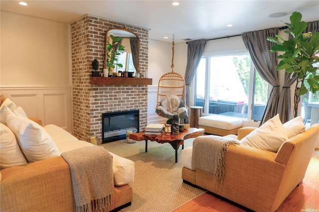 living area with recessed lighting, a wainscoted wall, a decorative wall, wood finished floors, and a brick fireplace