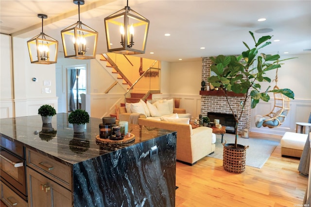 kitchen with decorative light fixtures, a fireplace, light wood finished floors, a decorative wall, and wainscoting