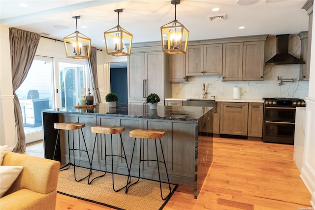 kitchen with visible vents, a sink, wall chimney range hood, double oven range, and a kitchen bar