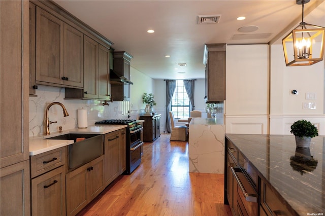 kitchen featuring range with two ovens, visible vents, light wood-style floors, a sink, and light stone countertops