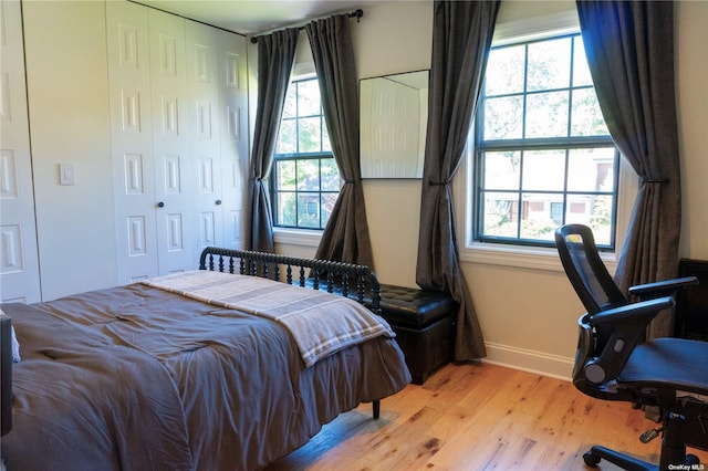 bedroom with light wood-style floors, a closet, multiple windows, and baseboards