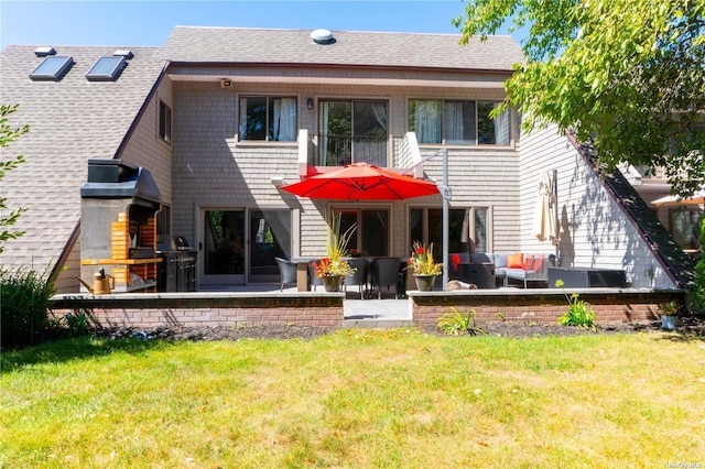 rear view of property featuring a balcony, a patio area, a lawn, and roof with shingles