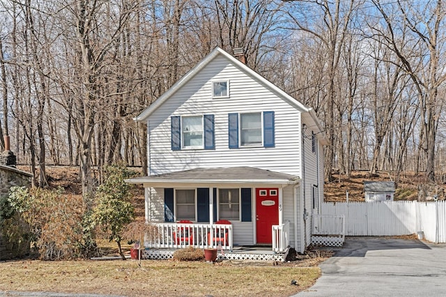 view of front of house featuring a front lawn, a gate, fence, covered porch, and a chimney