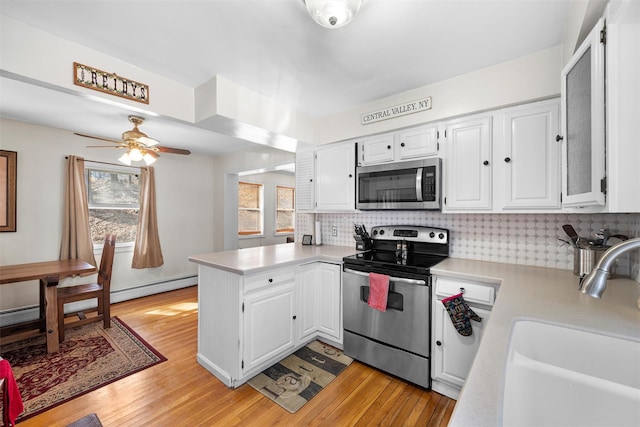 kitchen with light countertops, a peninsula, white cabinets, stainless steel appliances, and a sink