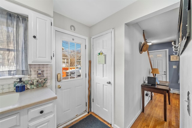 doorway featuring light wood finished floors, baseboards, and a baseboard radiator