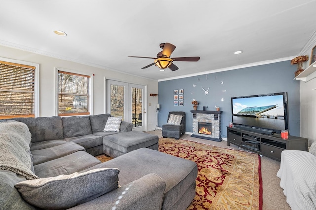 carpeted living room with a stone fireplace, baseboards, ceiling fan, and ornamental molding