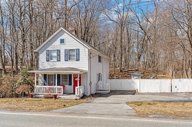 view of front of property with covered porch, a chimney, and fence