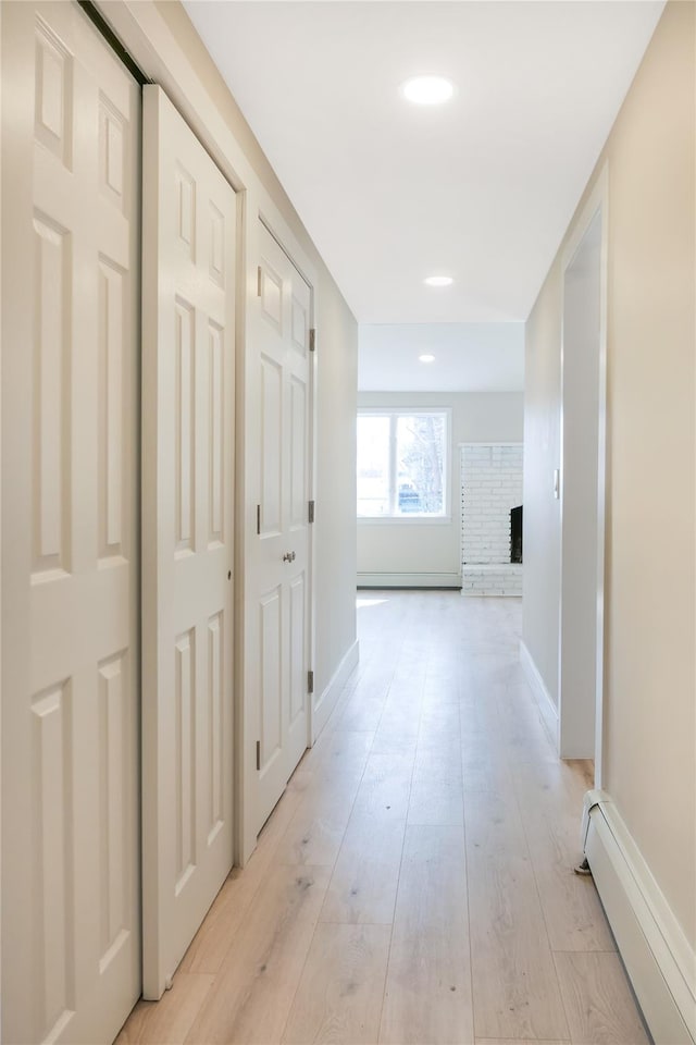 hall with a baseboard heating unit, recessed lighting, light wood-style floors, and baseboards