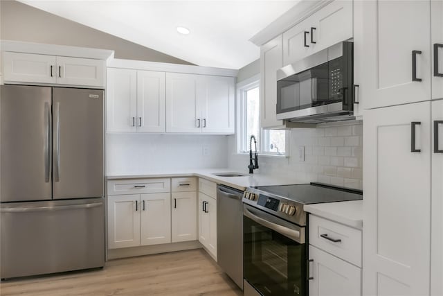 kitchen with light countertops, appliances with stainless steel finishes, white cabinets, vaulted ceiling, and a sink