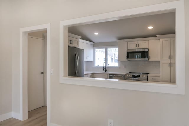 kitchen featuring decorative backsplash, light wood-style flooring, stainless steel appliances, white cabinetry, and a sink