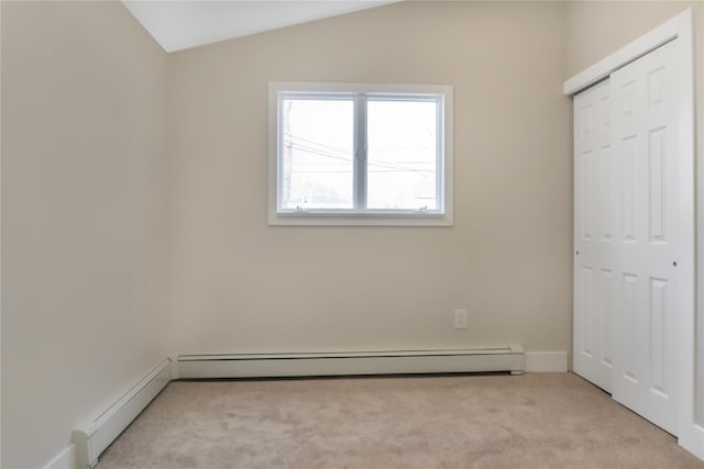 unfurnished bedroom with lofted ceiling, baseboard heating, a closet, and light colored carpet