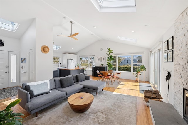 living room featuring high vaulted ceiling, a skylight, a fireplace, and light wood finished floors