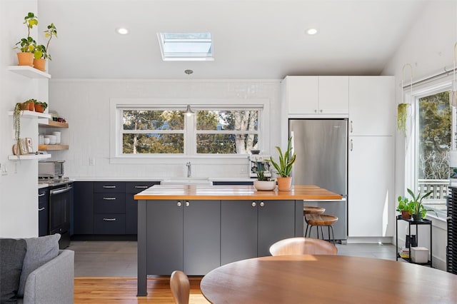 kitchen with open shelves, electric range oven, a skylight, freestanding refrigerator, and a sink