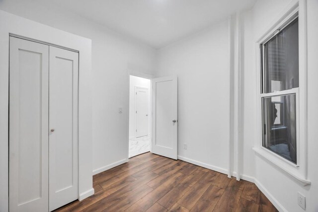 unfurnished bedroom with dark wood-style flooring, a closet, and baseboards