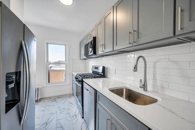 kitchen featuring marble finish floor, stainless steel appliances, gray cabinets, radiator, and a sink