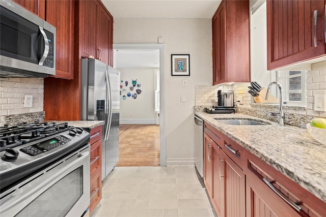 kitchen with appliances with stainless steel finishes, decorative backsplash, a sink, and light stone countertops