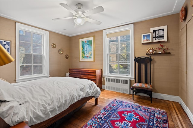 bedroom featuring baseboards, wood finished floors, a ceiling fan, and radiator