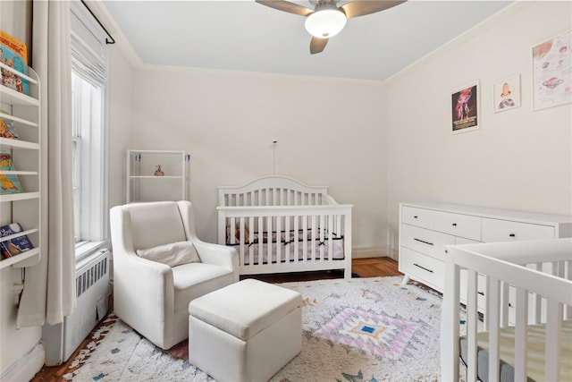 bedroom featuring a nursery area, wood finished floors, and a ceiling fan