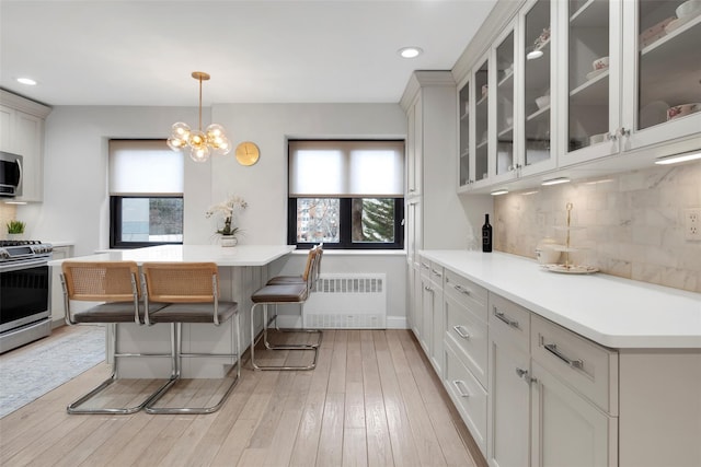 kitchen featuring decorative backsplash, radiator heating unit, stainless steel appliances, light countertops, and light wood-style floors