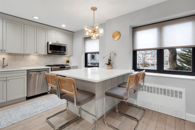 kitchen featuring a sink, a kitchen breakfast bar, appliances with stainless steel finishes, backsplash, and radiator heating unit