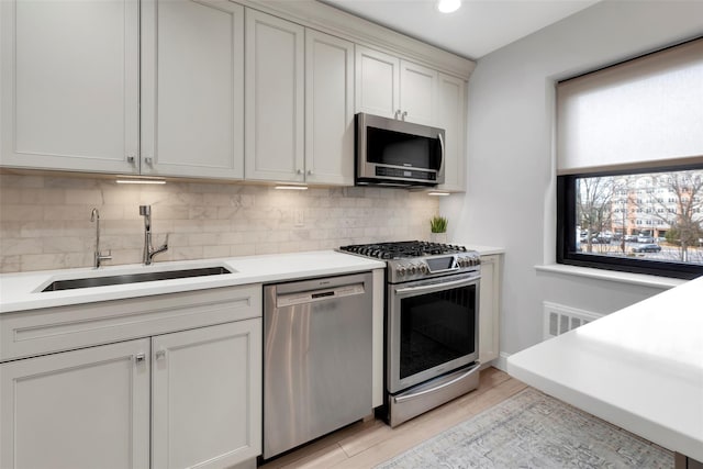 kitchen with stainless steel appliances, a sink, light wood-style floors, light countertops, and decorative backsplash