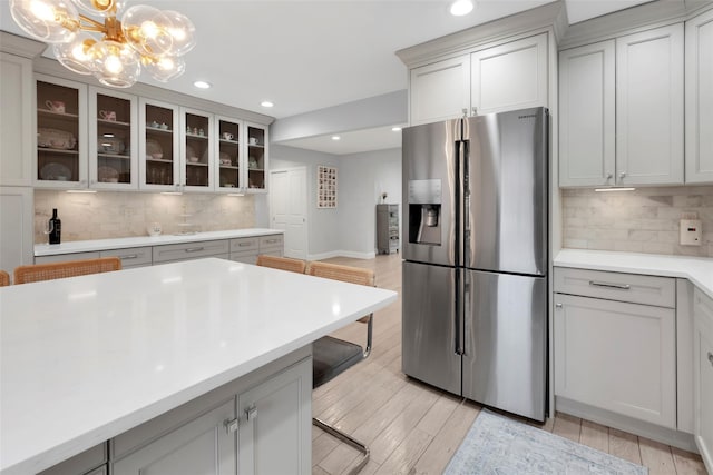 kitchen with light countertops, tasteful backsplash, stainless steel fridge, and light wood-style flooring